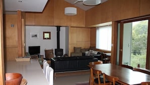 A modern living room with a sofa, TV, fireplace, and dining area with chairs and a table. - The Architects House - Architecturally designed home in a scrubland setting with native birdlife and a bush track to the beach (Marion Bay)