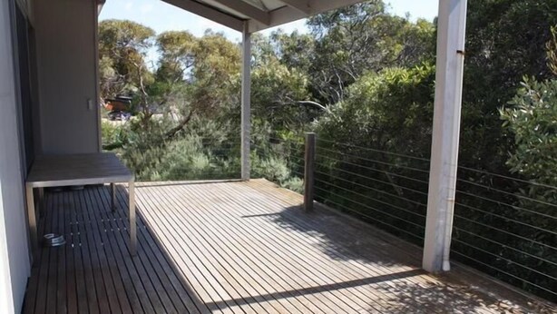A wooden deck with a metal railing, surrounded by dense foliage. - The Architects House - Architecturally designed home in a scrubland setting with native birdlife and a bush track to the beach (Marion Bay)