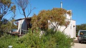 A white building with a chimney, surrounded by greenery and a parked vehicle. - The Architects House - Architecturally designed home in a scrubland setting with native birdlife and a bush track to the beach (Marion Bay)