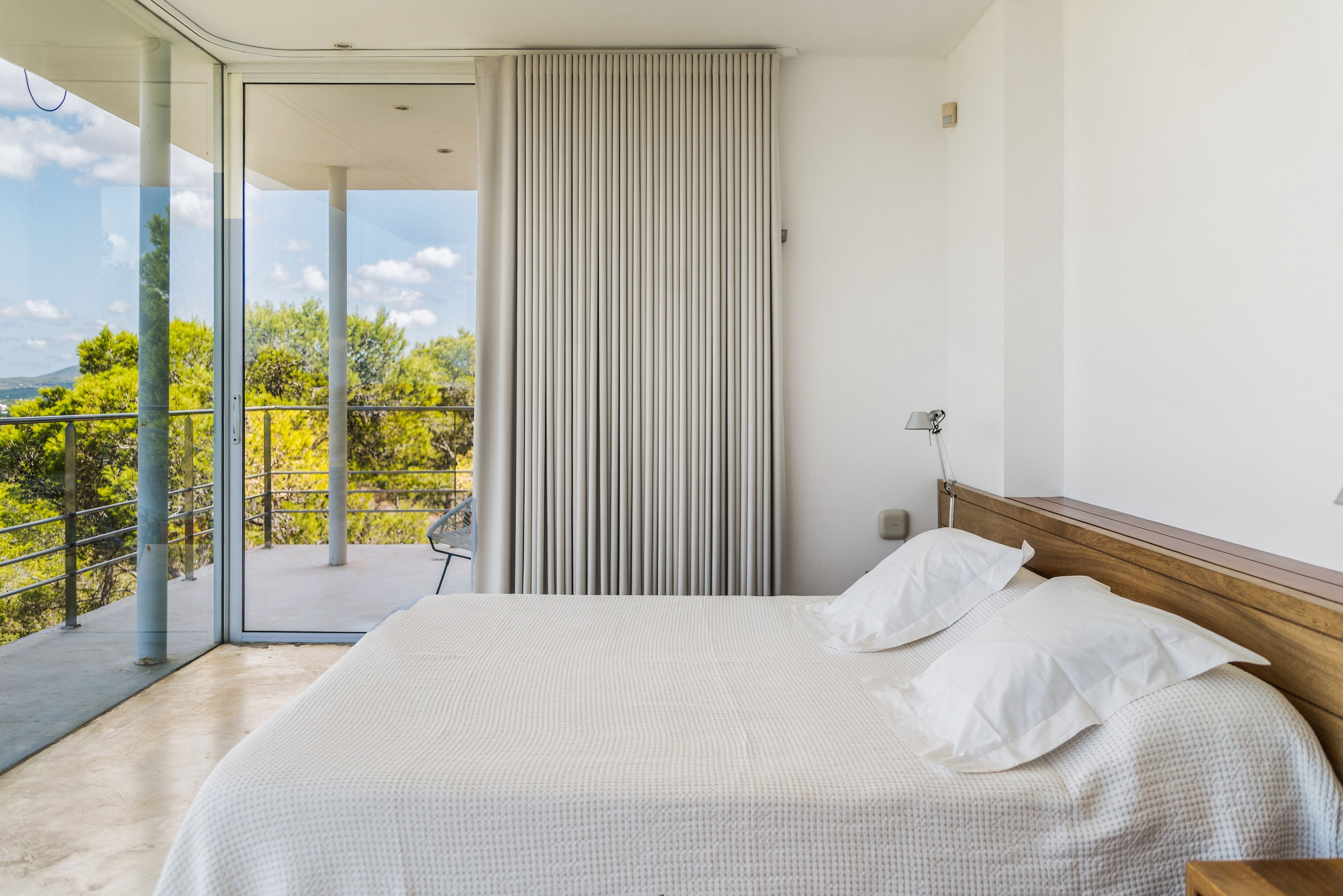 Une chambre d’hôtel avec un grand lit, une vue sur la verdure et un balcon doté d’une balustrade.