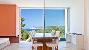 Un espace de repas moderne avec une grande table et des chaises, une vue sur la mer et un balcon agrémenté d’un canapé.
