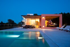 Ein modernes Haus mit Swimmingpool, Sitzgelegenheiten im Freien und einem gut beleuchteten Innenraum.
