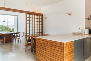 Cozinha moderna com ilha de madeira, área de refeições com cadeiras e vista através de uma porta de vidro.