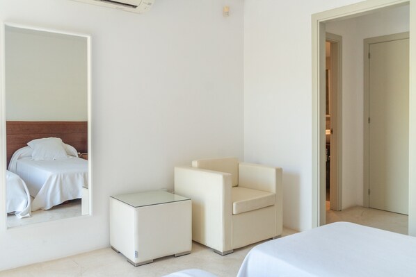 Habitación de hotel con cama, una silla, una mesita y un espejo. Se ve una puerta que conduce a otra habitación.