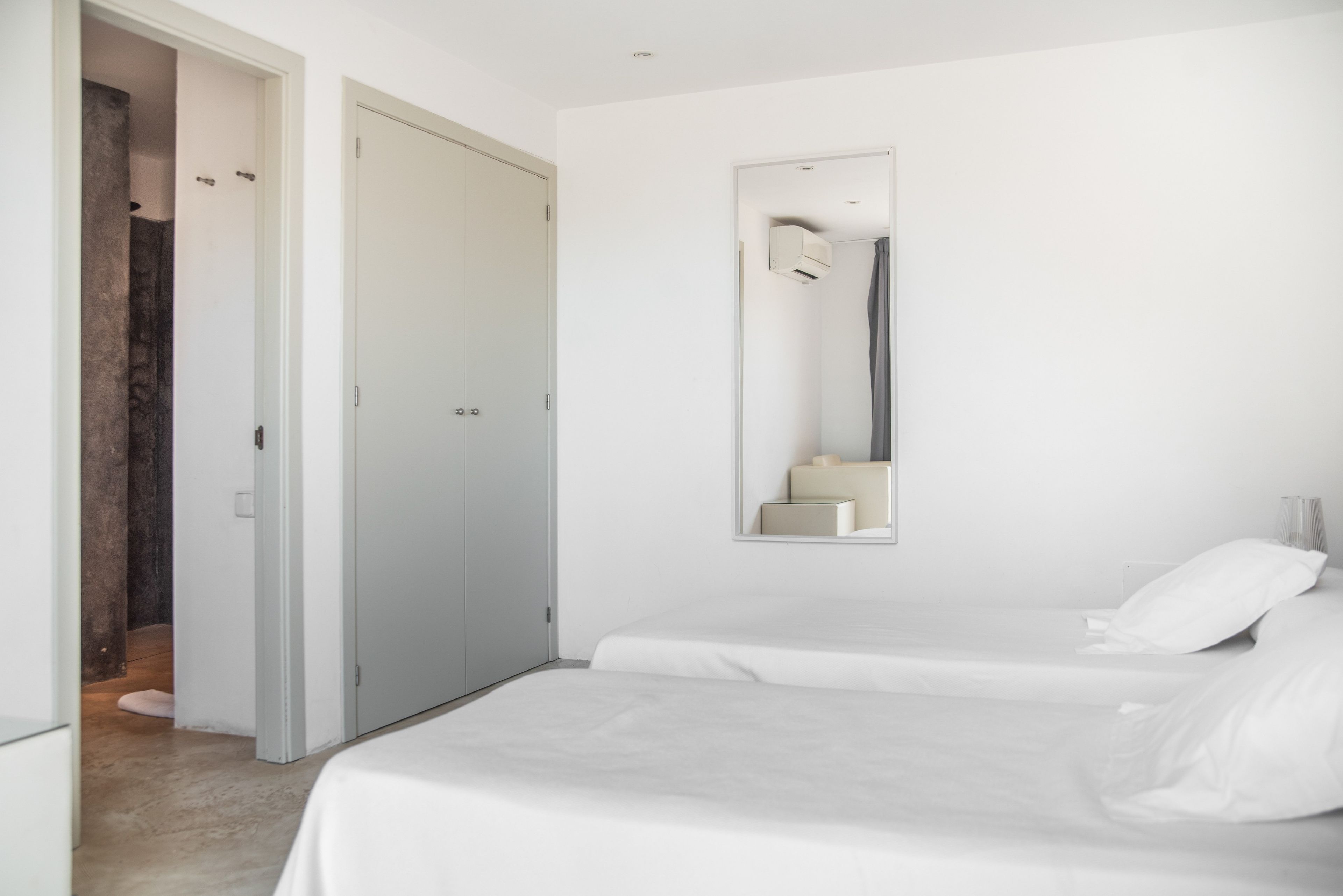 Un dormitorio minimalista con una cama doble, un espejo grande y una puerta que da a un baño.