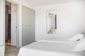 A minimalist bedroom with a double bed, a large mirror, and a door leading to a bathroom.