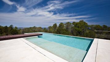 A rectangular swimming pool with clear water, surrounded by a concrete deck and a wooden deck on one side.