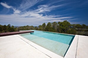 Ein rechteckiger Pool mit klarem Wasser, umgeben von einer Beton- und einer Holzterrasse.
