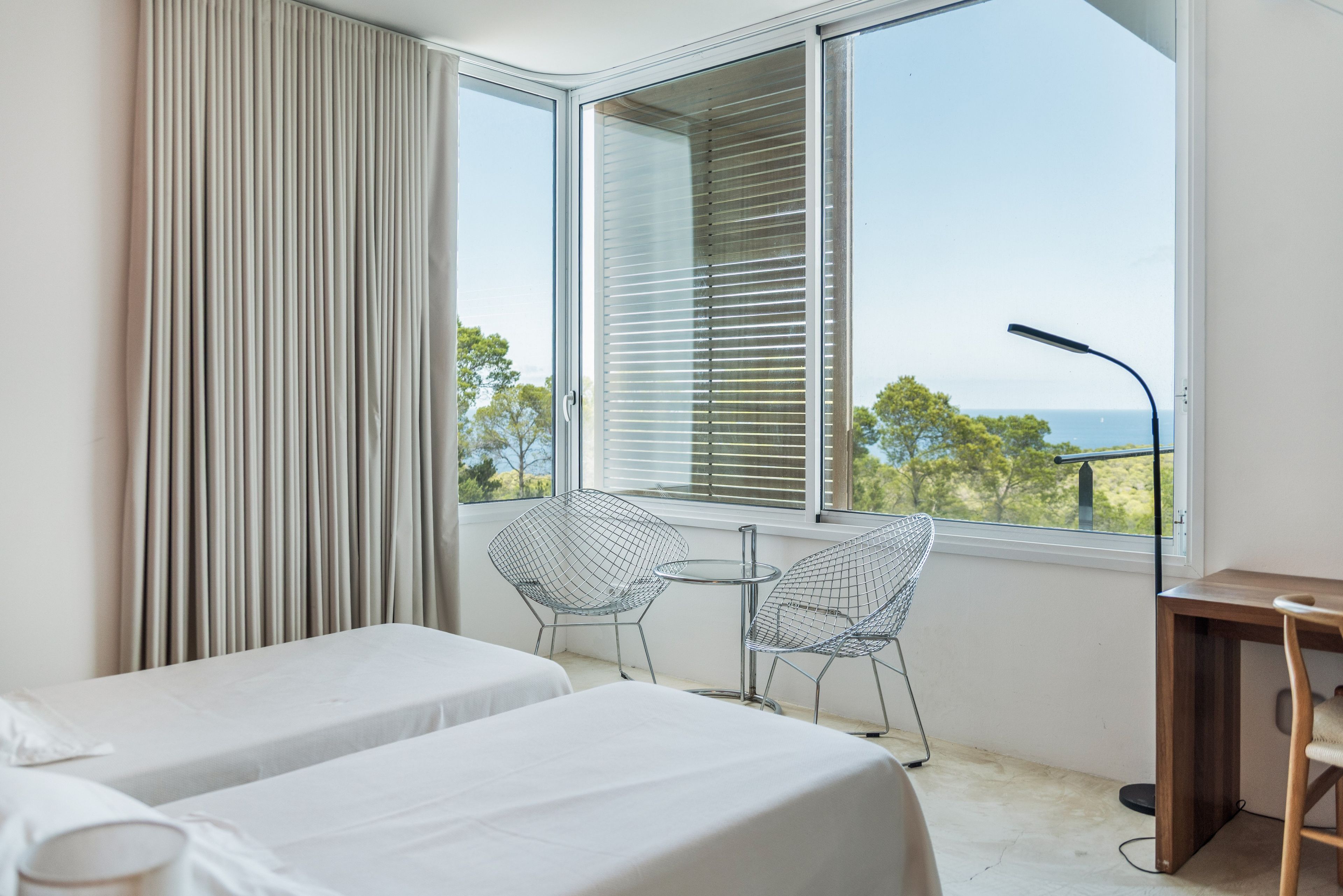 Une chambre d’hôtel avec deux lits, une fenêtre avec des stores, une chaise et un bureau.