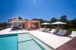 Ein moderner Poolbereich mit Liegestühlen und Sonnenschirmen, einer gläsernen Struktur und blauem Himmel.