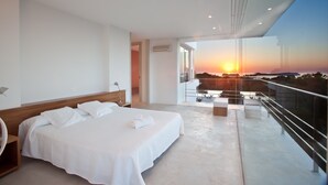 Une chambre d’hôtel moderne dotée d’un grand lit, d’un balcon offrant une vue sur le coucher de soleil et d’une entrée séparée.