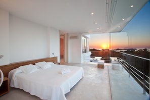 Une chambre d’hôtel moderne dotée d’un grand lit, d’un balcon offrant une vue sur le coucher de soleil et d’une entrée séparée.