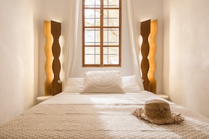 A bedroom with a bed, a window, and a woven hat on the bed.