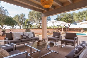 An outdoor patio area with a sofa, chairs, a glass coffee table, and umbrellas.