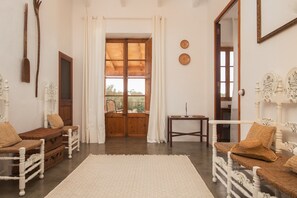 A room with a wooden door, white curtains, wicker furniture, and a white rug.