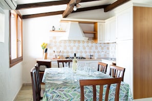 A kitchen with white cabinets, a tiled backsplash, a dining table set with chairs, and a window on the left.