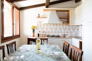 A dining area with a table set for four, a bottle of wine, and a kitchen in the background.