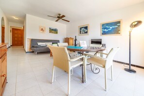 Una habitación con una mesa de comedor, sillas, un sofá, un ventilador de techo, obras de arte en las paredes y un cartel de bienvenida.