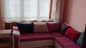 Una habitación acogedora con un sofá rosa, una mesita y una ventana con cortinas traslúcidas.