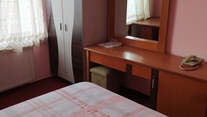 Una habitación con cama, escritorio de madera, espejo, armario y teléfono.