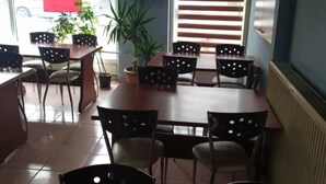 Un comedor con una mesa grande, sillas, plantas en macetas y una ventana con persianas.