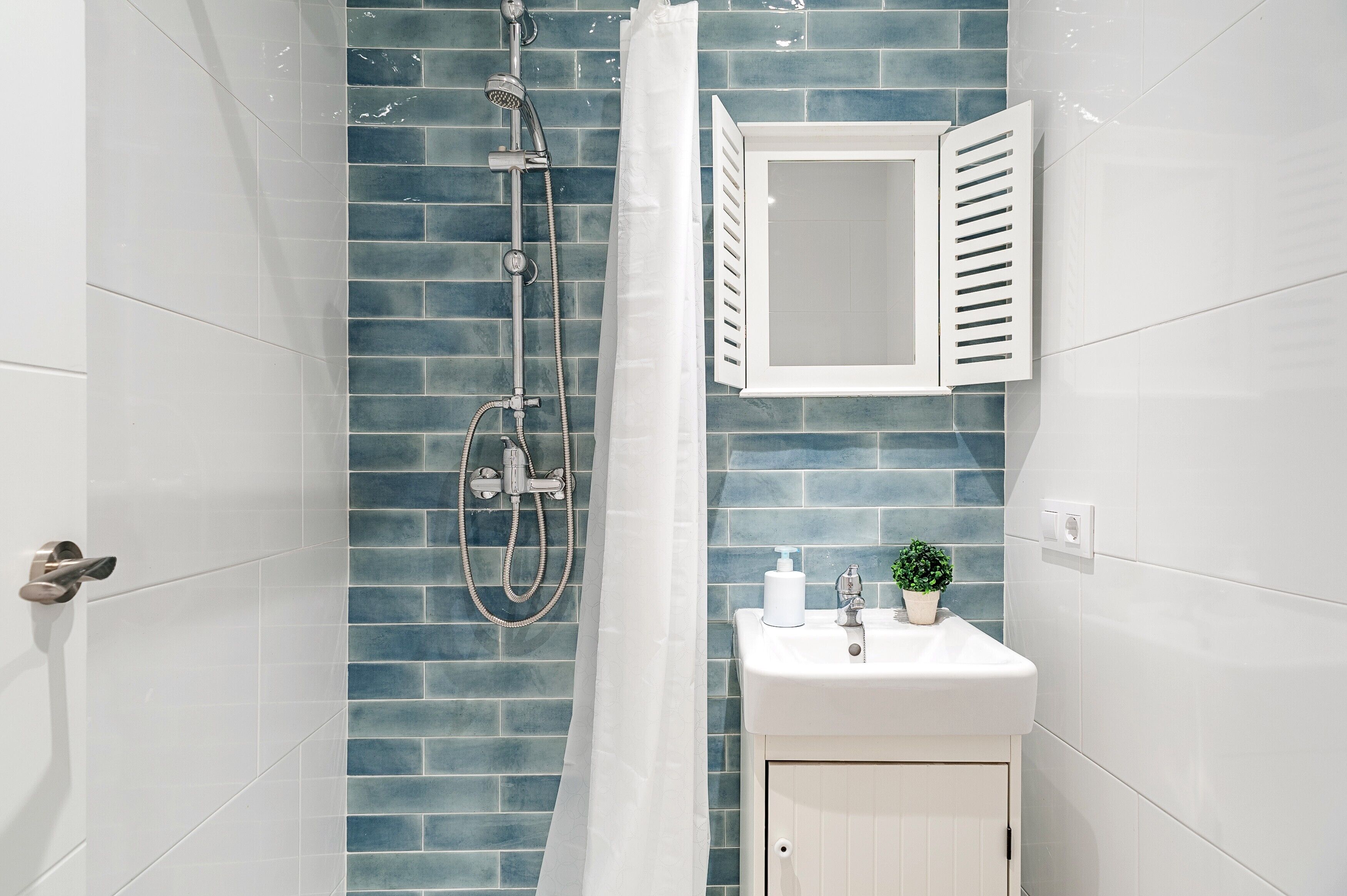 Een badkamer met een douche, wastafel, spiegel en een plant in pot.