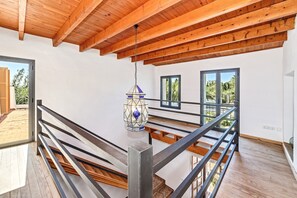 Ein modernes Interieur mit Holzbalkendecke, einer Treppe mit Metallgeländern und einer hängenden Leuchte.