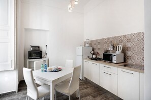 A modern kitchen with white cabinetry, a dining table with chairs, a microwave, a refrigerator, and a patterned backsplash.