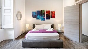 Ein Hotelzimmer mit einem Bett, zwei Nachttischen mit Lampen, einem großen Kunstwerk an der Wand und einer Tür.
