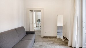 Ein Flur mit einem grauen Sofa, einem großen Spiegel und einer Tür zu einem weiteren Raum.