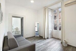 A modern living room with a grey sofa, a mirror, and a view through a door to an outdoor balcony.