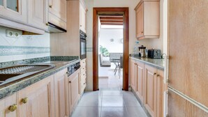 Een smalle keuken met houten kastjes, een inbouwoven en een aanrecht met een spoelbak.