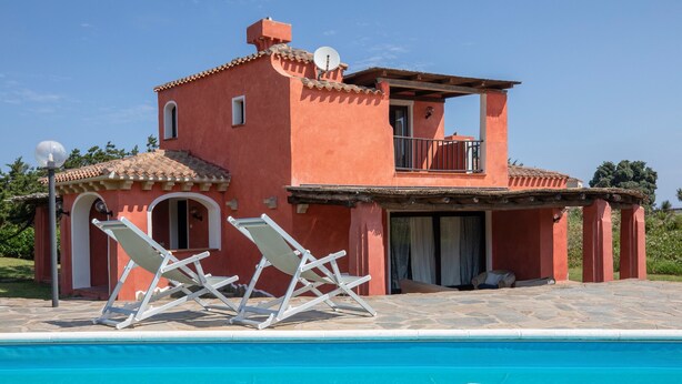 Una casa de dos pisos con piscina, balcón y puerta que da a un patio cubierto.