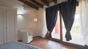Un dormitorio con cama, una silla, un armario, una ventana con cortinas y un balcón.