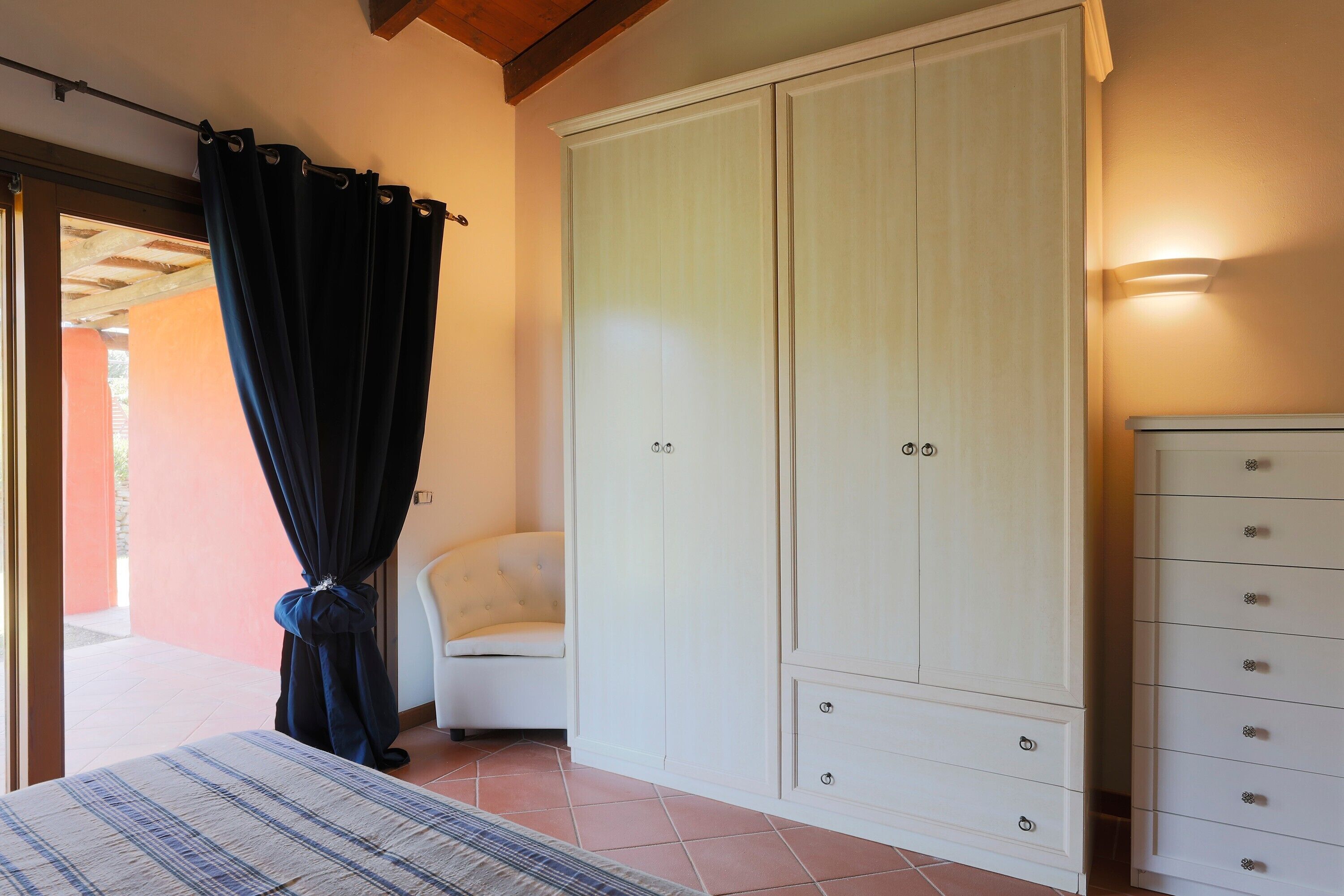 A bedroom with a bed, a white wardrobe, a chair, and a curtain.