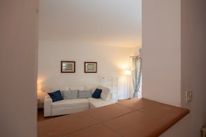 A living room with a white sofa, two framed pictures on the wall, a floor lamp, and a window with curtains.