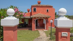 Una villa roja con tejado de tejas, un camino de piedra que lleva a la entrada y un patio con sillas.