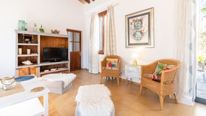 A living room with a TV, wicker chairs, a white sofa, and a wooden TV stand. - Villa Marilen near Can Picafort Beach with Mountain Views, Wi-Fi and A/C (SANTA MARGALIDA)