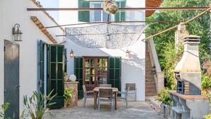 A patio with a table and chairs, a hanging lantern, and a stone fireplace. - Villa Marilen near Can Picafort Beach with Mountain Views, Wi-Fi and A/C (SANTA MARGALIDA)