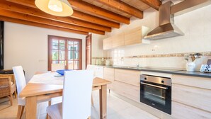 A modern kitchen with wooden beams, a dining table with chairs, and a built-in oven. - Villa Marilen near Can Picafort Beach with Mountain Views, Wi-Fi and A/C (SANTA MARGALIDA)