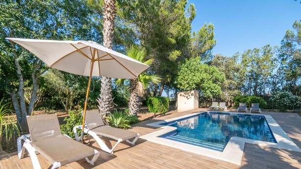 A swimming pool with lounge chairs and an umbrella, surrounded by trees and a tiled deck. - Villa Marilen near Can Picafort Beach with Mountain Views, Wi-Fi and A/C (SANTA MARGALIDA)