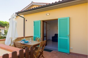 Uma área de refeições ao ar livre com mesa, cadeiras e um guarda-sol branco.