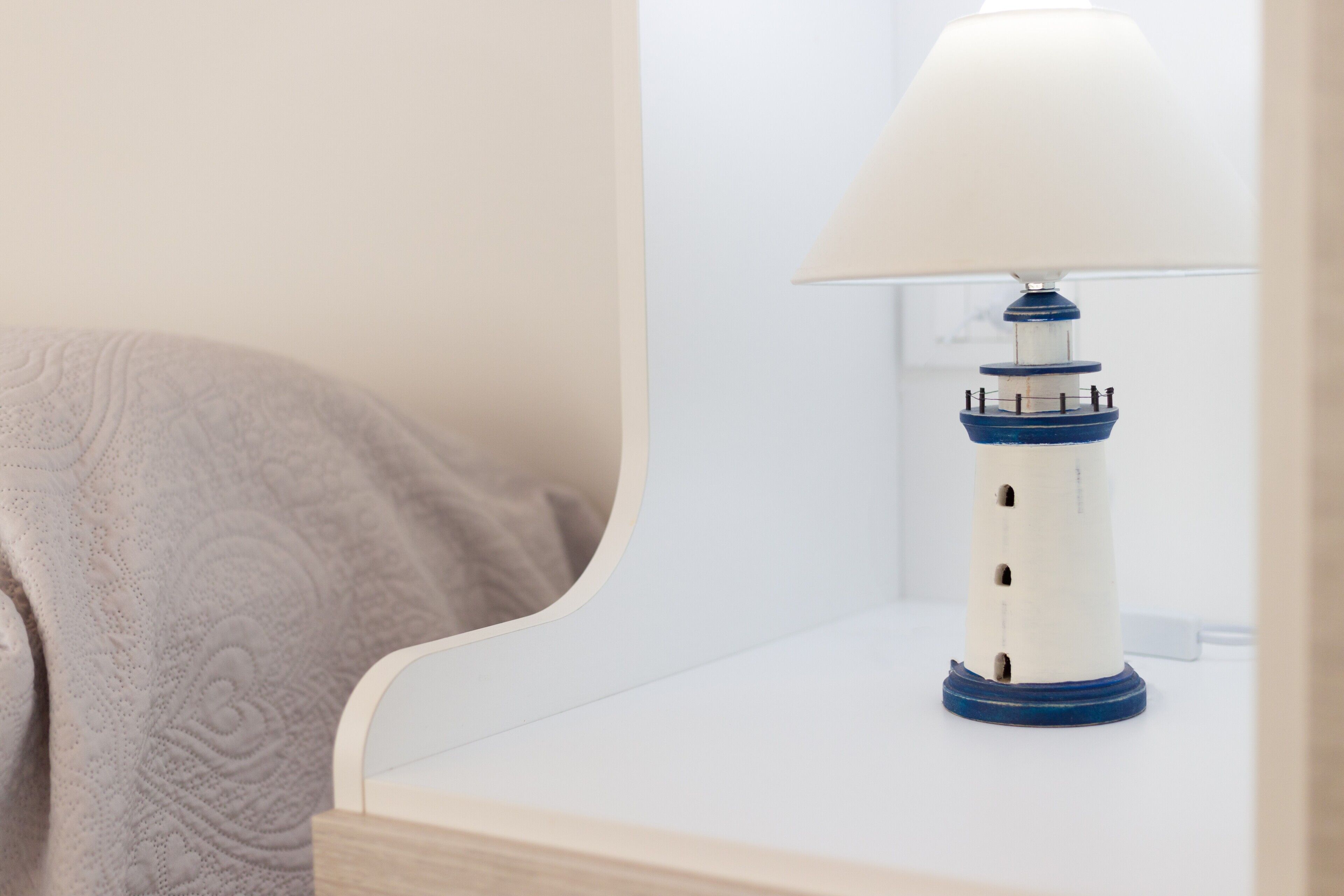 A bedside table with a lamp, a towel, and a wall-mounted outlet.
