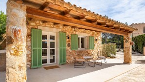 Ein Steinhaus mit einer Holz-Pergola, grünen Fensterläden und Korbmöbeln.