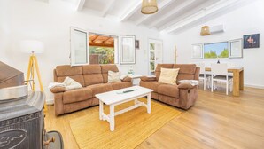 Ein Wohnzimmer mit zwei braunen Sofas, einem weißen Couchtisch, Holzboden, Deckenventilator und einem Fenster mit Blick auf Grünflächen.