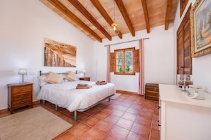 Een slaapkamer met een bed, nachtkastjes, een raam met gordijnen, een houten plafond en een schilderij aan de muur.