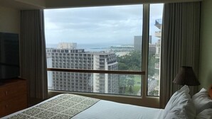 Een hotelkamer met een groot raam, een bed met witte lakens, een televisie op een houten dressoir en een lamp op het nachtkastje.