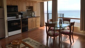 Een keuken met houten kasten, een eettafel met stoelen en uitzicht op de oceaan door grote ramen.