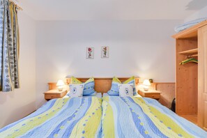 A bedroom with a bed, two bedside tables with lamps, a wooden wardrobe, and two wall-mounted pictures.