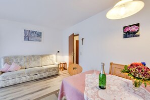 A living room with a sofa, a dining table with a bottle and flowers, and a guitar.